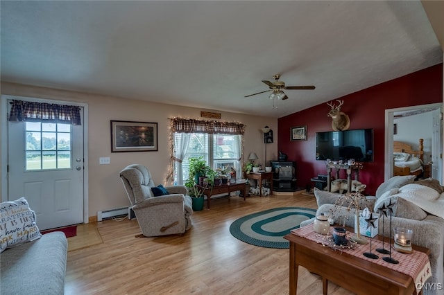 living room with a baseboard radiator, lofted ceiling, a wood stove, ceiling fan, and light hardwood / wood-style flooring