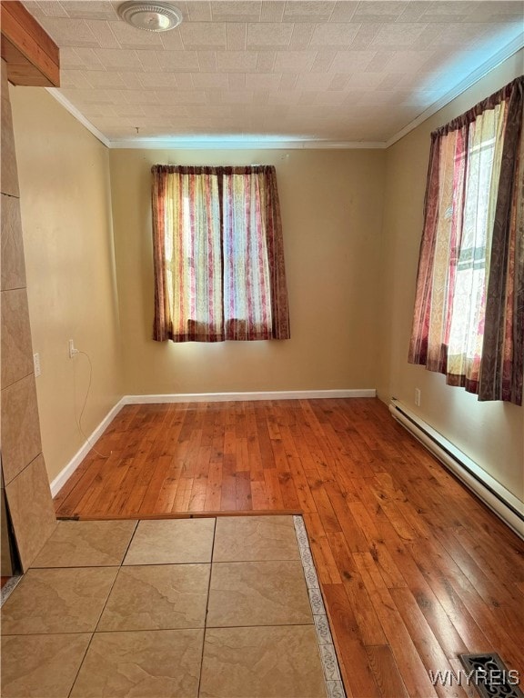 spare room with baseboard heating, ornamental molding, and wood-type flooring