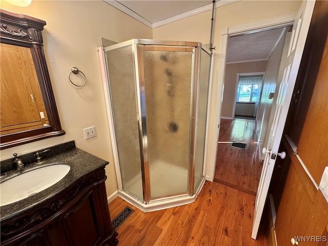 bathroom with vanity, ornamental molding, a shower with shower door, and hardwood / wood-style flooring