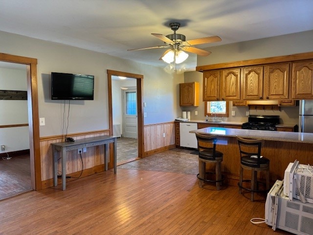 kitchen with black stove, white dishwasher, hardwood / wood-style floors, ceiling fan, and wooden walls