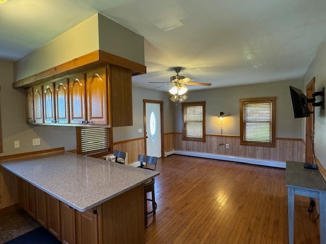 kitchen featuring baseboard heating, a breakfast bar area, kitchen peninsula, hardwood / wood-style floors, and ceiling fan