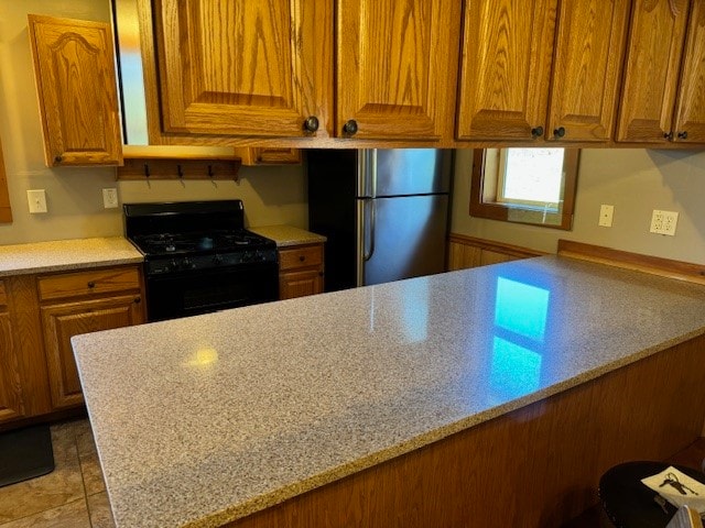 kitchen with black range with gas stovetop, light stone counters, and stainless steel fridge