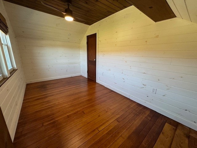 spare room with wooden walls, dark wood-type flooring, wooden ceiling, vaulted ceiling, and ceiling fan