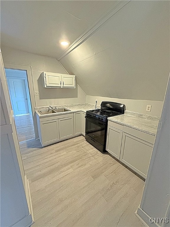 kitchen featuring sink, black gas stove, white cabinetry, lofted ceiling, and light hardwood / wood-style flooring