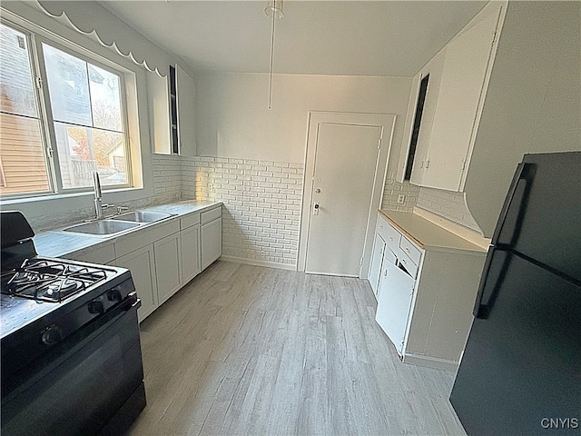 kitchen with sink, refrigerator, white cabinetry, and black gas range oven