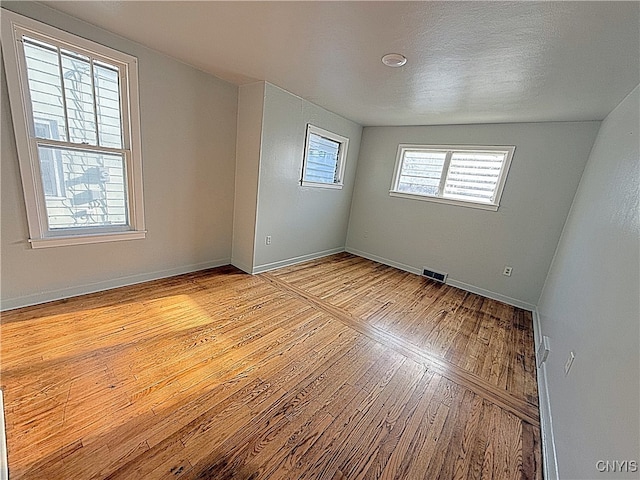 empty room with lofted ceiling, a textured ceiling, and light hardwood / wood-style flooring