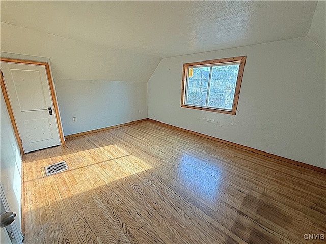 additional living space with light hardwood / wood-style flooring, a textured ceiling, and vaulted ceiling