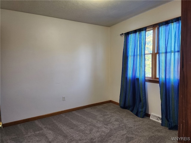 spare room with a textured ceiling and dark colored carpet