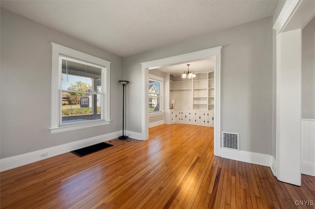 unfurnished room with hardwood / wood-style flooring, built in shelves, a textured ceiling, and a chandelier