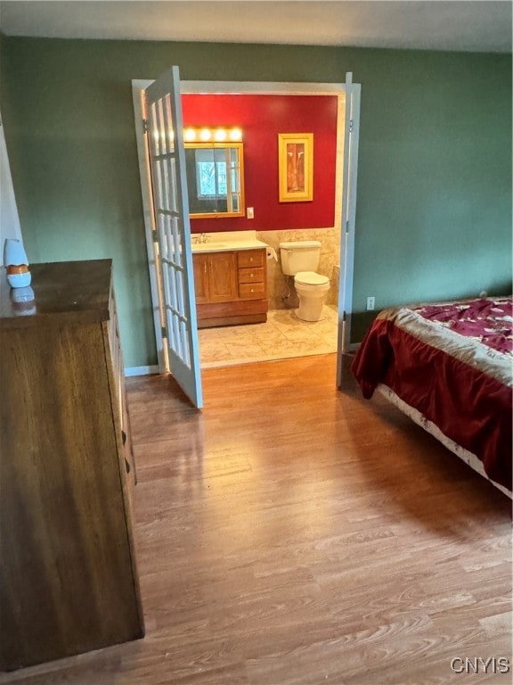 bedroom with ensuite bathroom, sink, and light wood-type flooring