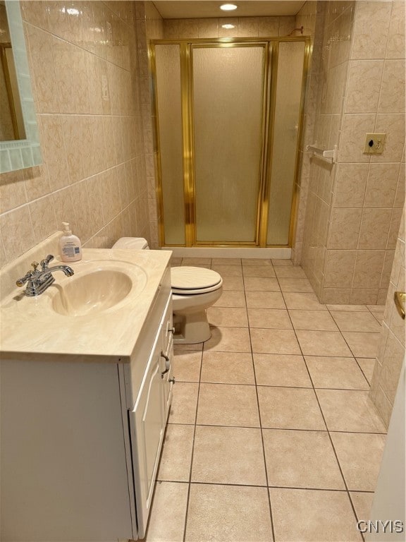 bathroom featuring a shower with door, vanity, tile patterned floors, toilet, and tile walls