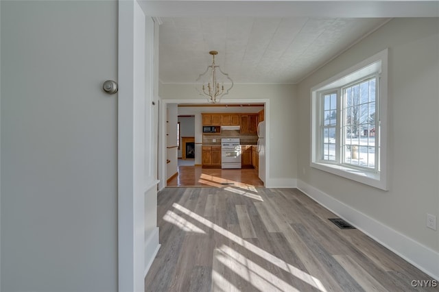 unfurnished dining area with ornamental molding, a chandelier, and light wood-type flooring