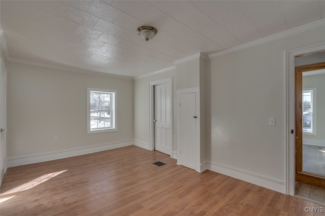 empty room featuring light hardwood / wood-style floors, crown molding, and plenty of natural light