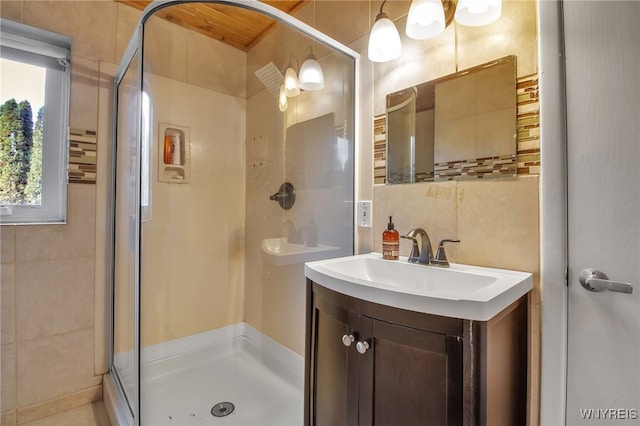 bathroom with a shower with door, vanity, and tile walls