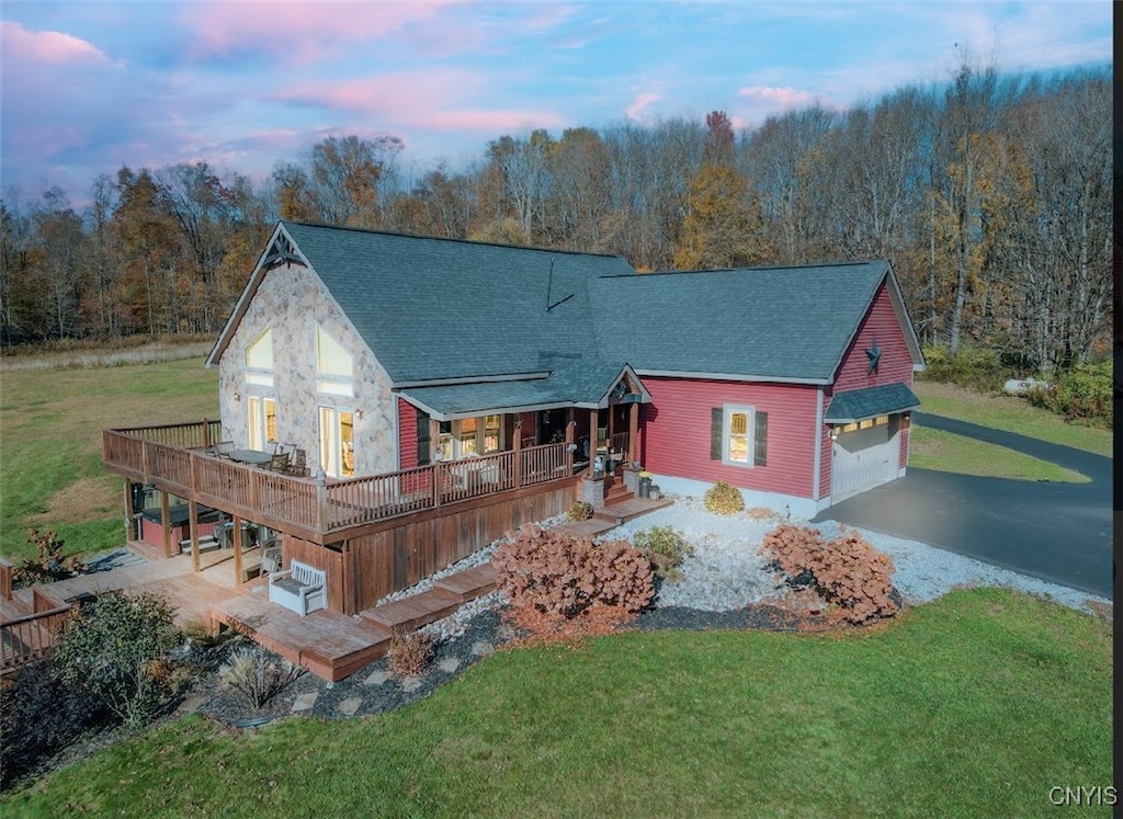 back house at dusk with a deck, a yard, and a garage