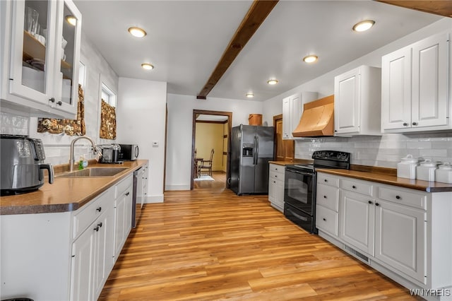 kitchen featuring appliances with stainless steel finishes, premium range hood, white cabinetry, light wood-type flooring, and sink