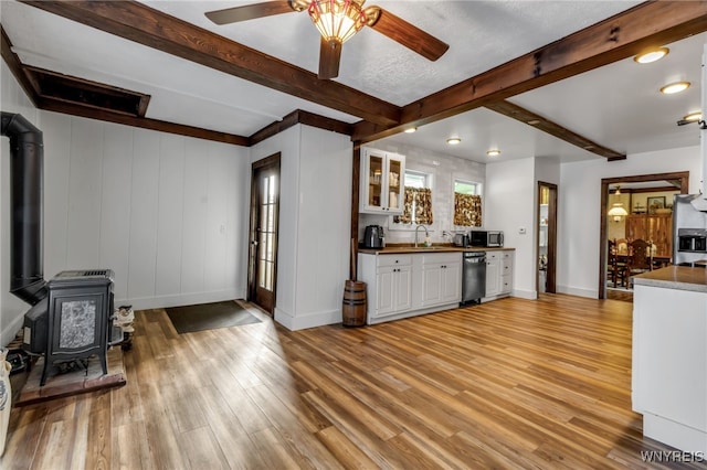 kitchen with dishwashing machine, ceiling fan, a wood stove, and light hardwood / wood-style flooring