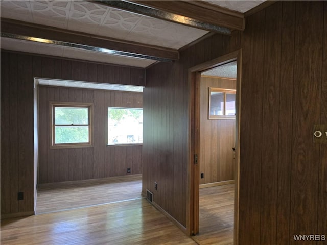 corridor with beam ceiling, wooden walls, and light hardwood / wood-style floors