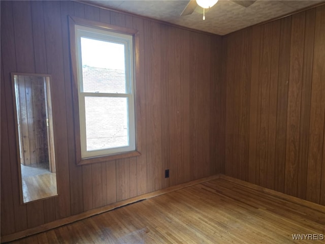 unfurnished room featuring light hardwood / wood-style flooring, wooden walls, and ceiling fan