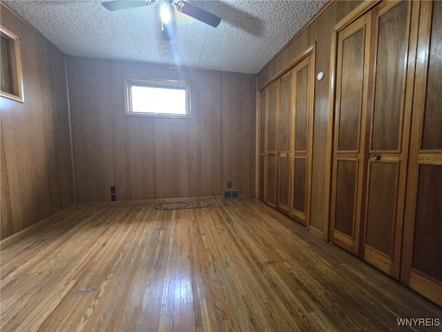 basement featuring wood walls, a textured ceiling, wood-type flooring, and ceiling fan