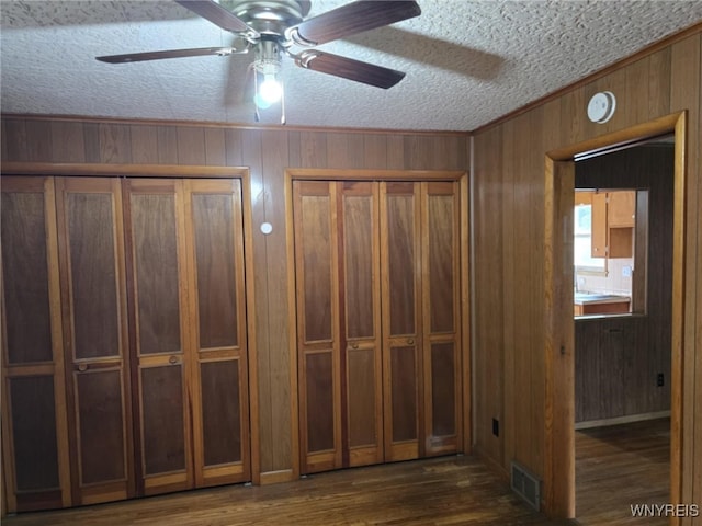 interior space with ceiling fan, a textured ceiling, dark hardwood / wood-style flooring, and wooden walls