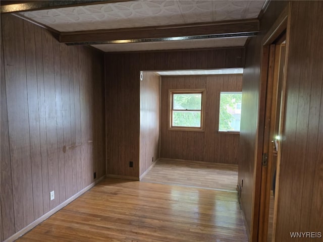 spare room featuring beamed ceiling, light wood-type flooring, and wood walls