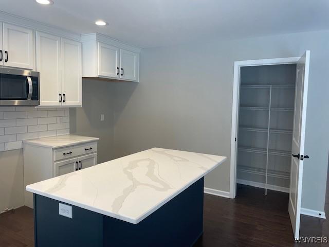 kitchen with light stone counters, dark wood-type flooring, white cabinets, stainless steel microwave, and tasteful backsplash