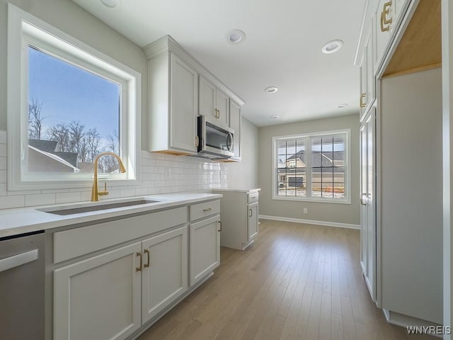 kitchen with light wood finished floors, a sink, decorative backsplash, light countertops, and appliances with stainless steel finishes