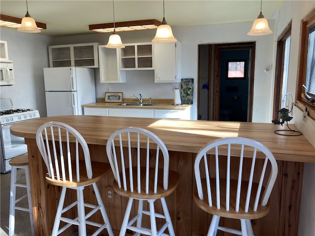 kitchen with white cabinets, a kitchen bar, white appliances, and sink