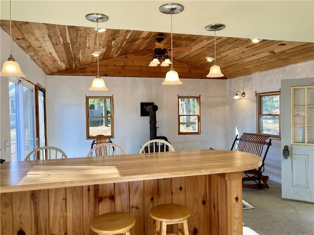 kitchen featuring a healthy amount of sunlight, a wood stove, hanging light fixtures, and vaulted ceiling