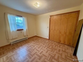 unfurnished bedroom with a closet, baseboard heating, and light parquet floors