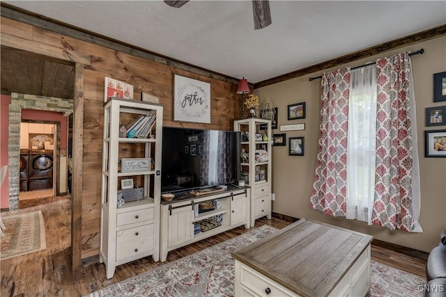 living room with ornamental molding, wood walls, wood finished floors, washing machine and dryer, and ceiling fan