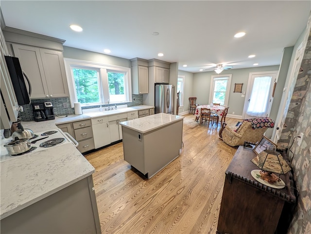 kitchen with light hardwood / wood-style flooring, gray cabinetry, a center island, light stone counters, and stainless steel refrigerator