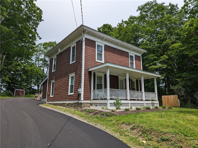 view of front of home featuring a storage shed, a front yard, and covered porch