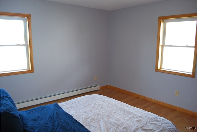 bedroom with a baseboard heating unit, multiple windows, and hardwood / wood-style flooring