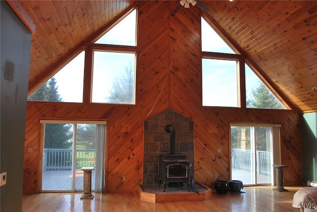 unfurnished living room featuring high vaulted ceiling, a healthy amount of sunlight, a wood stove, and wooden walls