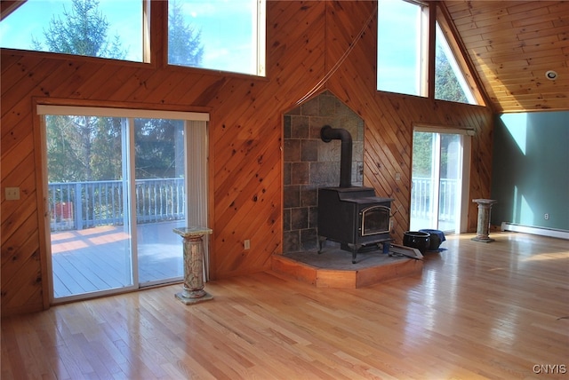 unfurnished living room featuring high vaulted ceiling, wood walls, a wood stove, and light hardwood / wood-style flooring