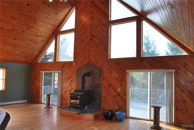 living room featuring a wood stove, high vaulted ceiling, a baseboard radiator, and a wealth of natural light