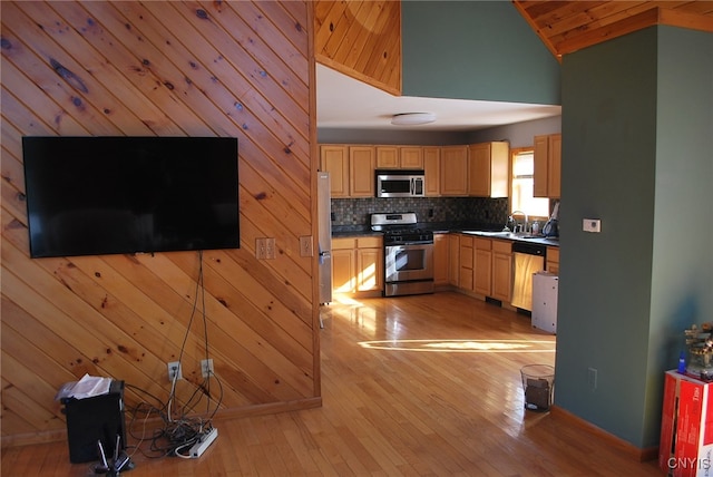 kitchen with stainless steel appliances, light wood-type flooring, light brown cabinetry, high vaulted ceiling, and wood walls