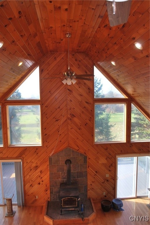 unfurnished living room featuring plenty of natural light, light wood-type flooring, a wood stove, and wood walls