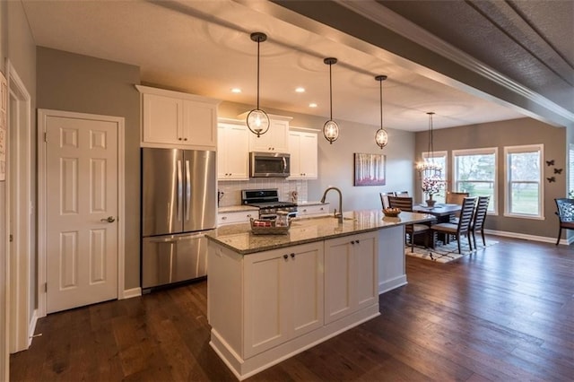 kitchen with a center island with sink, appliances with stainless steel finishes, white cabinetry, light stone counters, and dark hardwood / wood-style floors