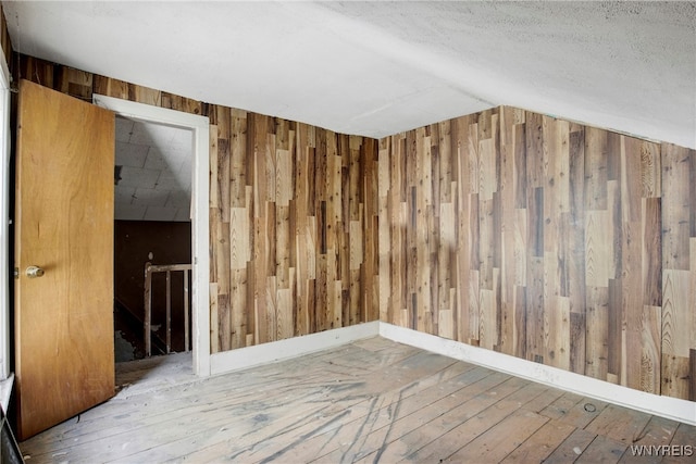 empty room featuring lofted ceiling, hardwood / wood-style flooring, and wooden walls