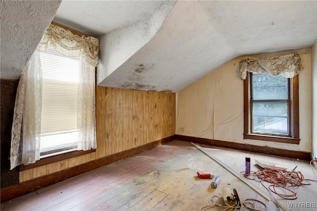 additional living space with lofted ceiling, hardwood / wood-style floors, a textured ceiling, and wood walls