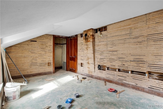 bonus room with vaulted ceiling and wood walls