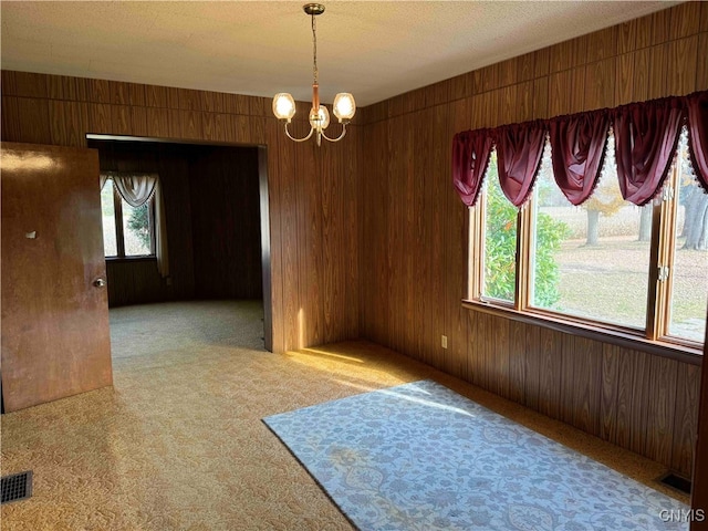 unfurnished room with light carpet, a notable chandelier, a textured ceiling, and wood walls