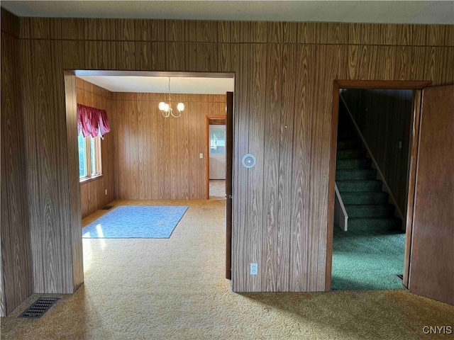 carpeted empty room with a notable chandelier and wooden walls