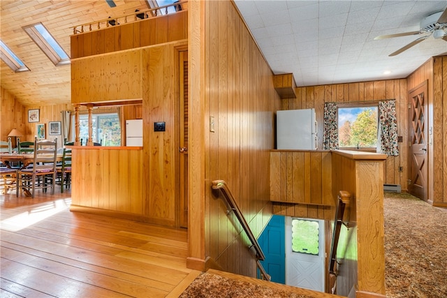 stairway featuring a skylight, a baseboard heating unit, ceiling fan, wooden walls, and hardwood / wood-style flooring