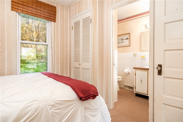 carpeted bedroom featuring a closet, ensuite bath, and tile walls