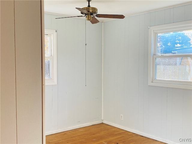 empty room with wood walls, light wood-type flooring, and ceiling fan