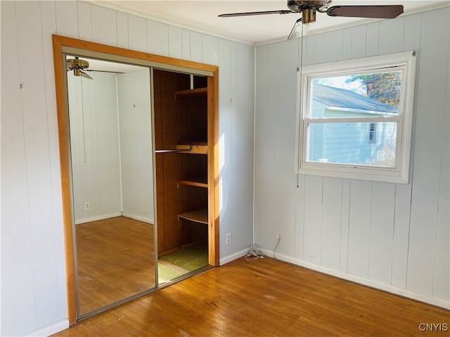 unfurnished bedroom with wooden walls, hardwood / wood-style floors, a closet, and ceiling fan